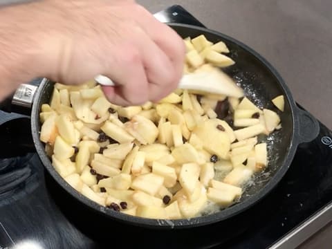 Les morceaux de pommes, le sucre en poudre et les raisins secs sont mélangés ensemble dans la poêle, à l'aide d'une spatule