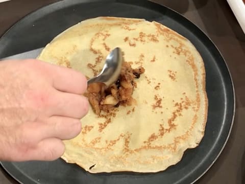 Une cuillère à soupe de compote de pommes est versée au centre de la crêpe qui est sur une plaque à pâtisserie ronde