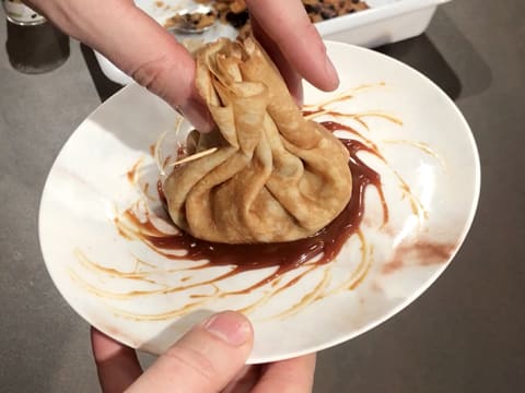 La crêpe aumonière est déposée au centre de l'assiette de service, sur la sauce au caramel qui forme un décor en forme de soleil