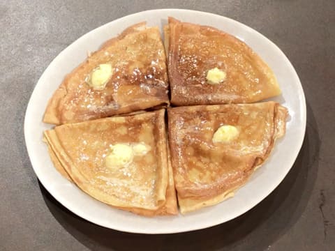 Une noix de beurre d'orange est déposée sur les quatre crêpes dans l'assiette