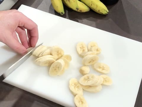 Une banane est coupée en rondelles à l 'aide d'un couteau, sur une planche à découper