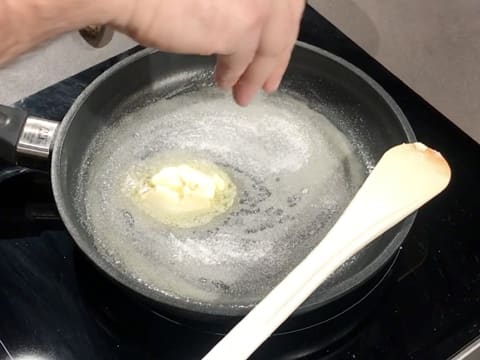 Du sucre en poudre est versé en pluie fine sur le beurre fondu, dans la poêle