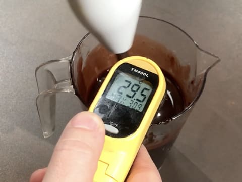 Prise de la température du glaçage chocolat qui se trouve dans le pichet verseur avec un thermomètre électronique qui affiche 29,5°C