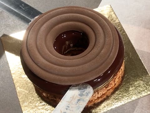 Le crémeux chocolat est déposé sur l'entremets glacé à l'aide de deux spatules métalliques coudées