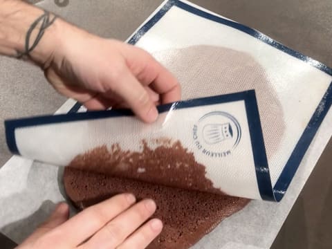 Le tapis de cuisson en silicone est retiré du biscuit chocolat qui est sur une feuille de papier sulfurisé sur le plan de travail