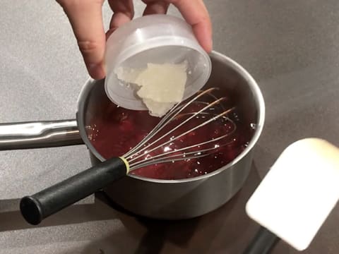 La gélatine hydratée est versée dans la casserole qui contient la préparation à base de purée de mangue et de griottes et qui est posée sur le plan de travail