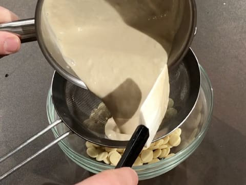 La crème chaude contenue dans la casserole est filtrée dans la passoire fine au-dessus du saladier qui contient les pistoles de chocolat blanc