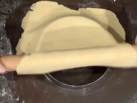 La pâte enroulée autour du rouleau à pâtisserie, est déroulée sur le cercle à mousse