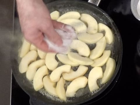 Les lamelles de pomme qui sont dans la poêle, sont saupoudrées de sucre en poudre