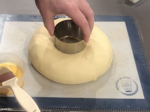 La pâte à brioche sur la plaque à pâtisserie recouverte du tapis de cuisson en silicone, a poussé autour du cercle à mousse qui est en train d'être retiré par le haut