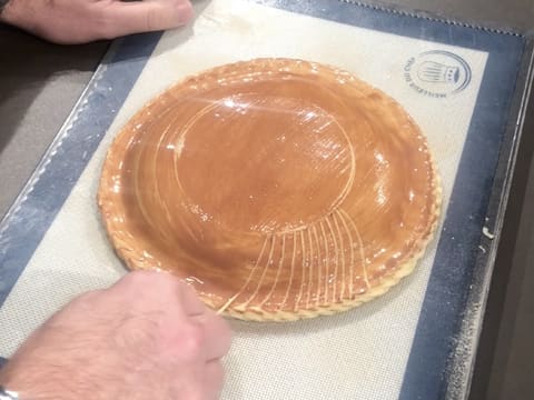 À l'aide d'un cure dent, des rainures sont dessinées tout autour de la marque ronde faite au centre de la galette qui est recouverte de dorure au cacao