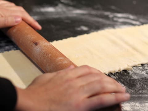 La pâte est abaissée en une longue bande avec le rouleau à pâtisserie sur le plan de travail fleuré