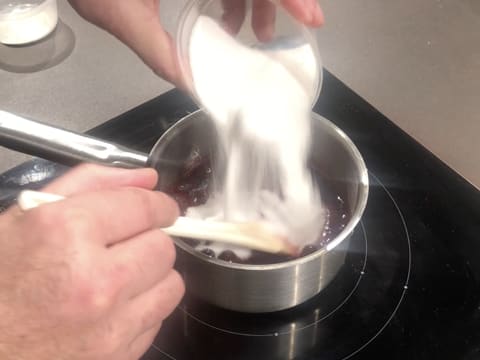 Ajout du sucre en poudre sur les myrtilles et la purée de cassis, dans la casserole posée sur la plaque de cuisson