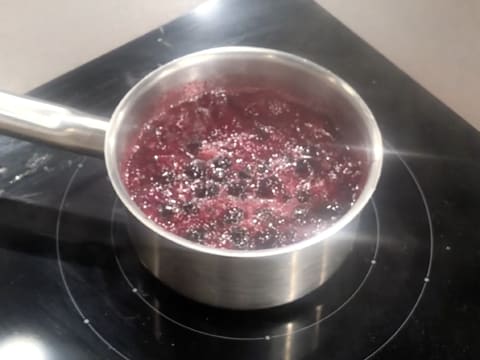 La préparation au cassis est en train de bouillir dans la casserole qui est placée sur la plaque de cuisson