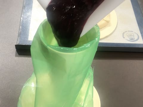 Le confit de cassis lissé est versé dans une poche pâtissière qui est maintenue par un support poche à douille