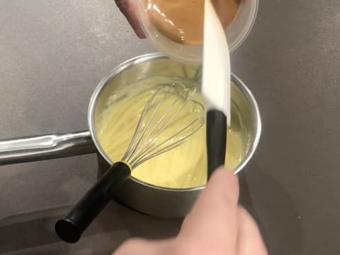 Ajout de la pâte de noisette dans la crème qui est dans la casserole posée sur le plan de travail