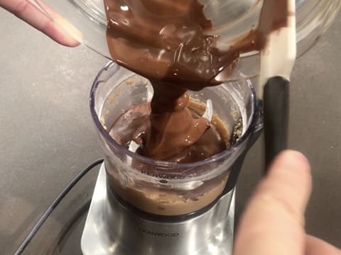 Le chocolat au lait fondu est versé sur la pâte de noisette qui se trouve dans la cuve du petit mixeur