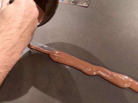 Le chocolat au lait tempéré est versé sur la bande de ruban pvc, sur le plan de travail