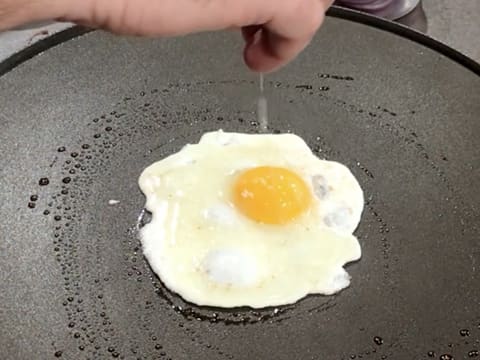 L'œuf qui est en train de cuire sur la crêpière électrique est assaisonné de sel fin