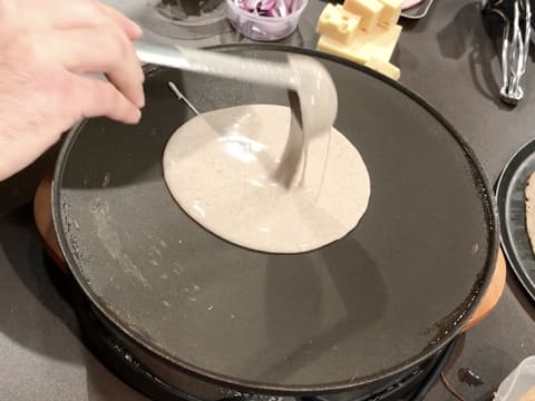 Une louche de pâte à galettes est versée sur la plaque de la crêpière électrique