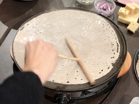 La pâte à galettes est étalée sur toute la surface de la crêpière à l'aide d'un râteau à crêpes en bois