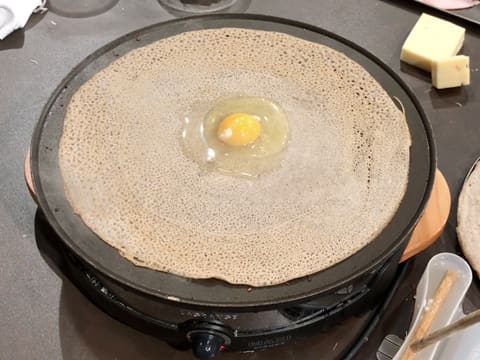 Un œuf est déposé au centre de la galette qui est en train de cuire sur la crêpière électrique