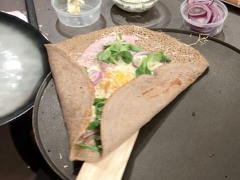 Obtention de la galette de sarrasin farcie avec oeuf, qui est saisie avec la spatule à crêpes en bois