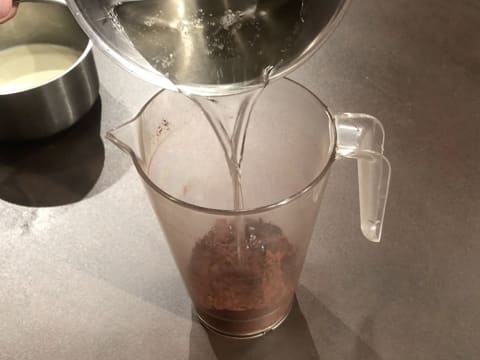 Le sirop bouillant est versé sur le cacao en poudre qui est dans le pichet verseur posé sur le plan de travail