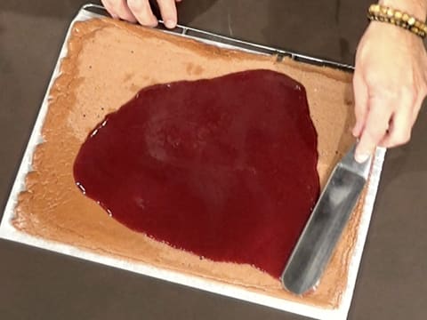 La compote de griotte est étalée sur le biscuit au chocolat à l'aide d'une spatule métallique coudée