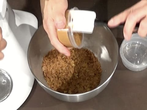 Le praliné noisette est versé dans la cuve du batteur, sur le crumble et le pailleté feuilletine