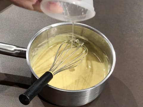 Ajout de la gélatine hydratée et fondue dans la crème qui est dans la casserole sur le plan de travail