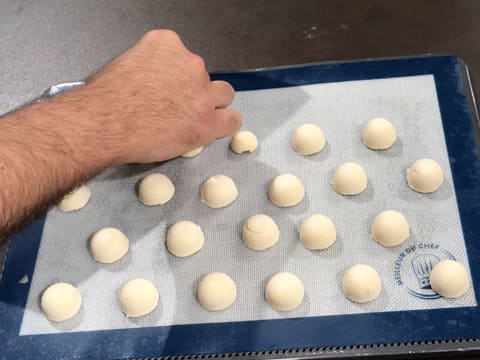 Des petites demi sphères de pâte à choux sont posées sur une plaque de cuisson perforée recouverte d'un tapis de cuisson en silicone