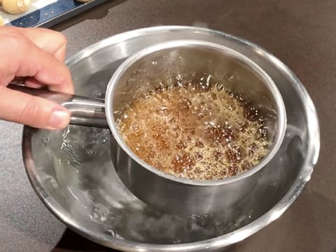 Le fond de la casserole qui contient le caramel doré et en ébullition, est plongé dans une bassine remplie d'eau