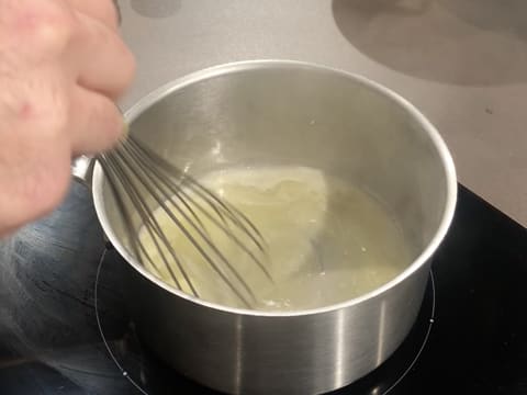 Le beurre est en train de fondre dans la casserole, tout en étant mélangé avec un fouet