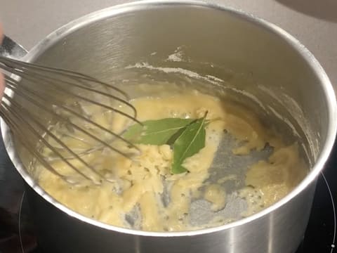 Ajout des feuilles de laurier sur l'ail haché et le roux blanc dans la casserole