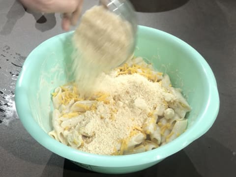 Ajout du parmesan râpé sur le cheddar râpé et les pâtes cuites et enrobées de sauce béchamel qui se trouvent dans le cul de poule posé sur le plan de travail