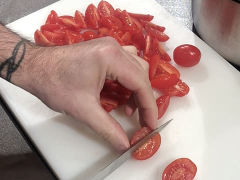 Les tomates cerises sont coupées en quartier à l'aide d'un couteau éminceur, sur une planche à découper