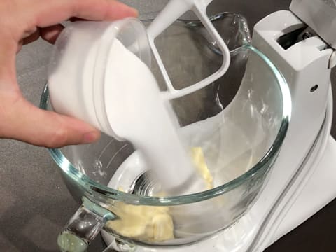 Ajout du sucre en poudre sur le beurre dans la cuve du batteur électrique qui est muni de l'accessoire crochet