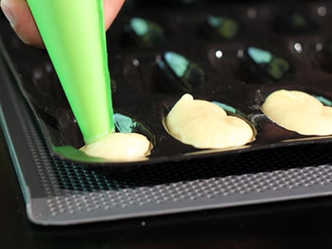 La pâte à madeleines est pochée dans les empreintes d'un moule à madeleines en silicone