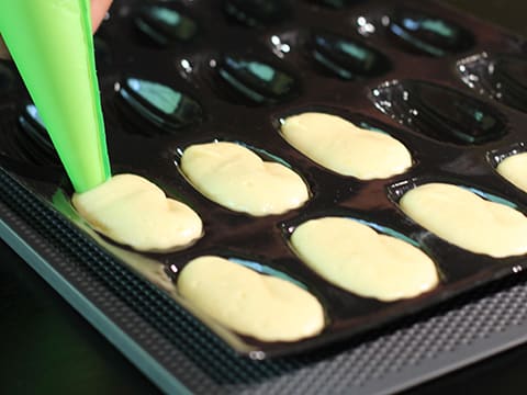 La pâte à madeleines est pochée dans les empreintes d'un moule à madeleines en silicone