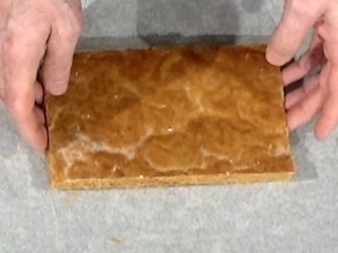 Une bande de pâte feuilletée cuite est placée sur une plaque à pâtisserie recouverte d'une feuille de papier sulfurisé