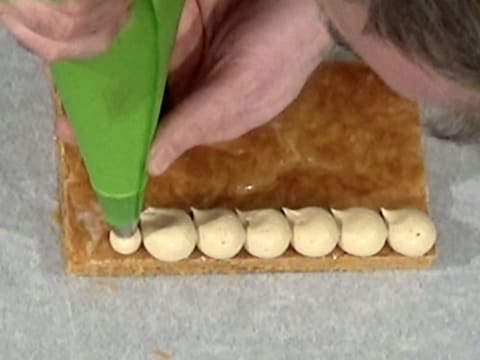 La crème mousseline café est pochée en forme de grosses gouttes sur un côté de la bande de pâte feuilletée cuite