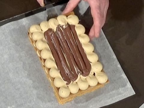 Une plaque de pâte feuilletée recouverte de mousseline café et de crémeux chocolat est déposée sur la seconde plaque à l'aide d'une spatule métallique coudée