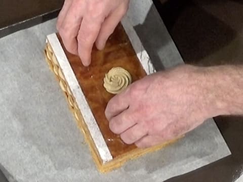 La plaque de pâte feuilletée ornée d'une rosace de crème mousseline café est pressée du bout des doigts sur les deux autres étages