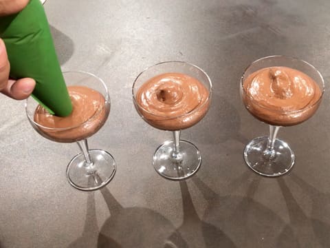 La mousse au chocolat noir est pochée dans des verrines à l'aide de la poche à douille