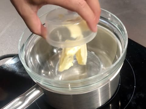 Du beurre est versé dans le saladier en verre qui est placé sur une casserole contenant de l'eau