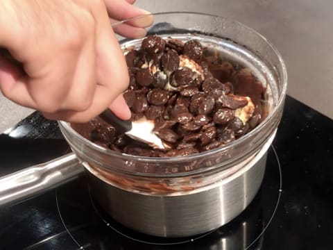 À l'aide d'une spatule maryse, mélange du chocolat noir et du beurre qui sont en train de fondre dans le saladier en verre qui est placé sur une casserole contenant de l'eau