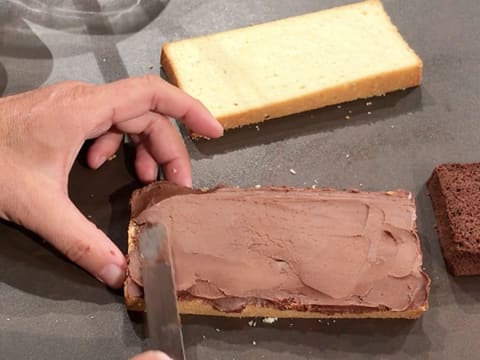 La ganache au chocolat est étalée sur la première tranche de génoise vanillée de façon uniforme, à l'aide d'une spatule coudée