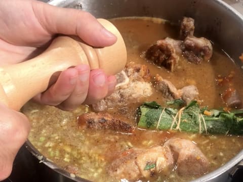 Assaisonnement de l'osso buco avec du poivre du moulin dans le faitout