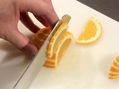 La moitié de l'orange est émincée en fines tranches à l'aide d'un couteau sur une planche à découper